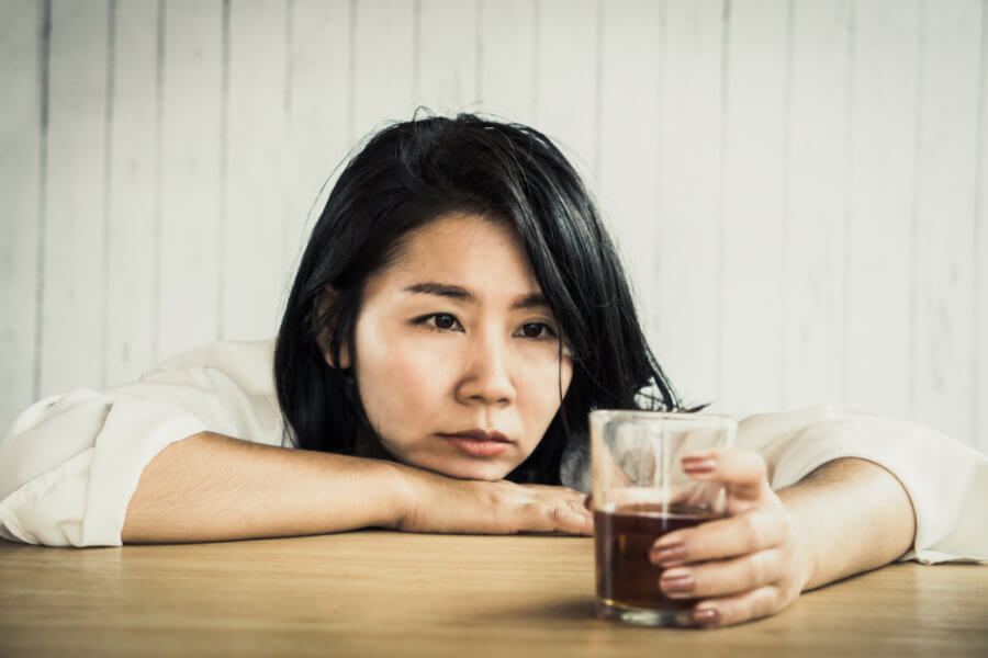 Woman with a chronic drinking issue and cardiomyopathy staring at glass of liquor