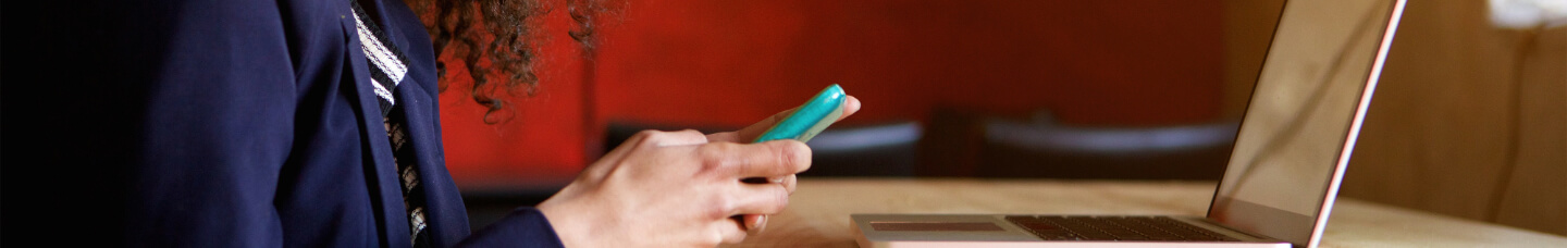 Woman reads small business news on her mobile device and laptop.