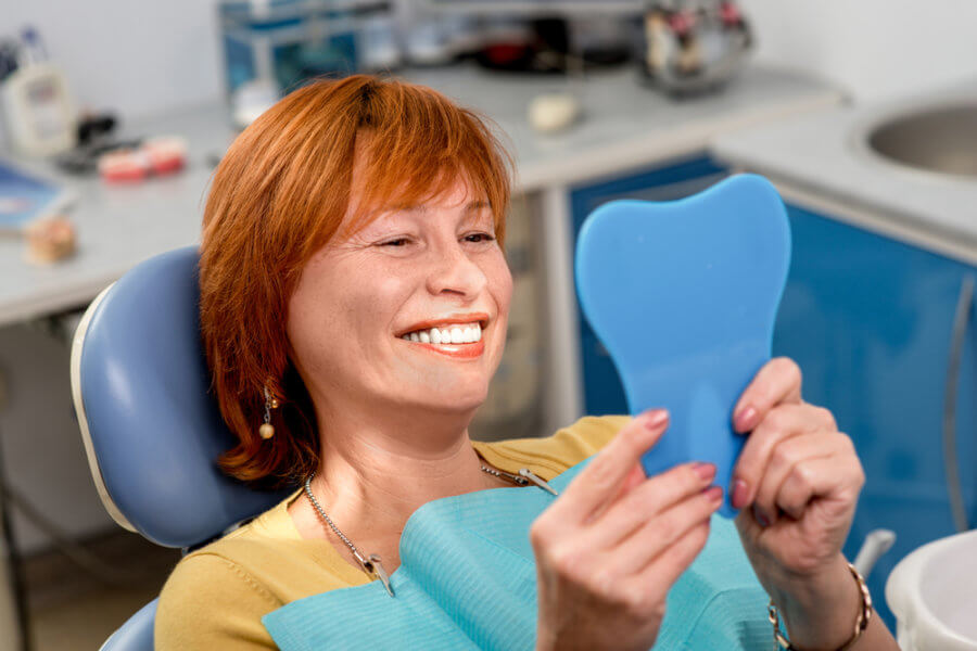 Woman looking in the mirror at her new implant supported dentures