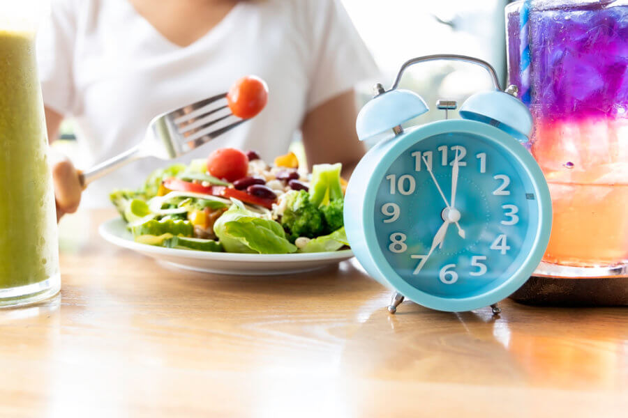 Woman eating salad next to a clock telling her when she can eat for intermittent fasting