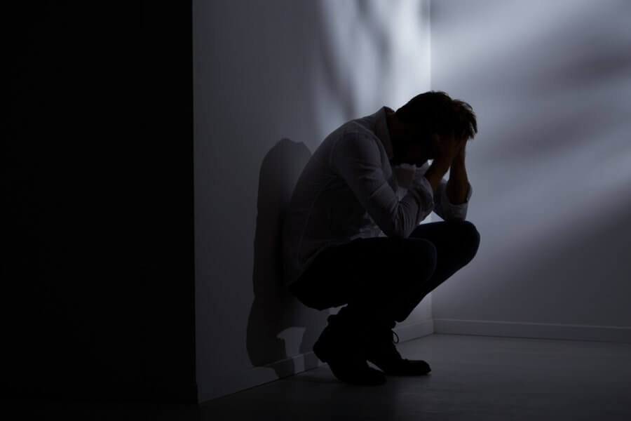 Depressed man sitting against a wall wondering if it is normal to have suicidal thoughts