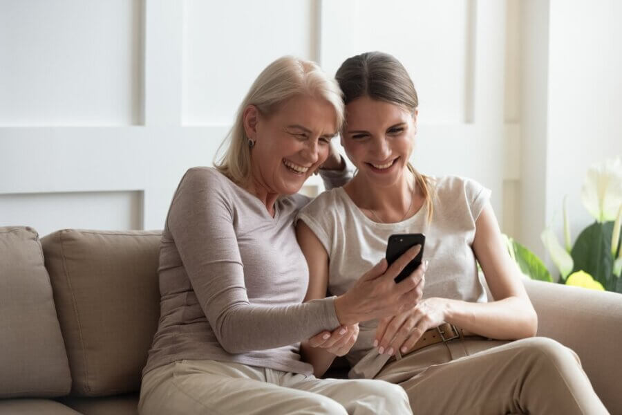 Older adult mother looks at mobile phone with daughter